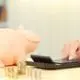 Person using a calculator that is lying next to a piggy bank and several stacks of coins.