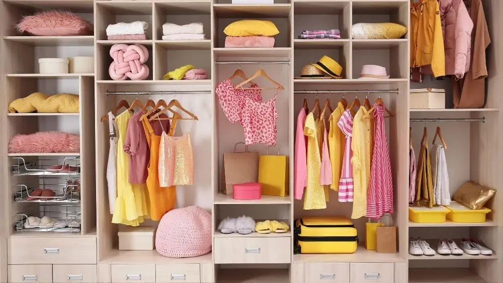 An organized closet with yellow and pink clothes hanging on rods or folded on shelves