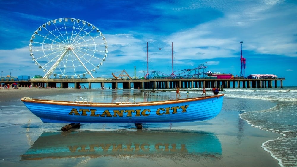 view of Atlantic City New Jersey beach with blue boat in foreground with the words Atlantic City on the side and a ferris wheel and boardwalk in background