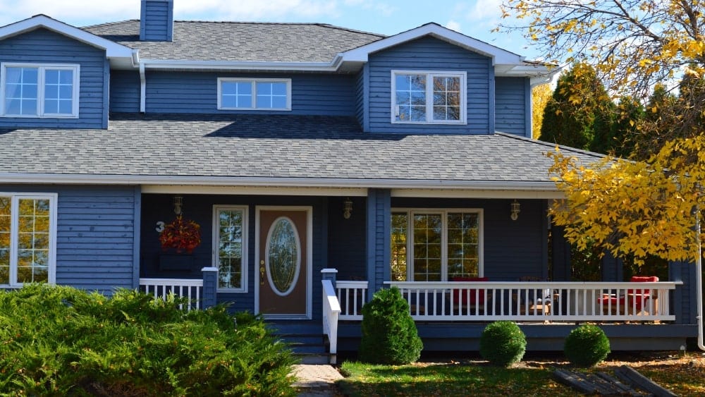 Two-story traditional home with blue painted exterior and porch with white railing and red door with oval window