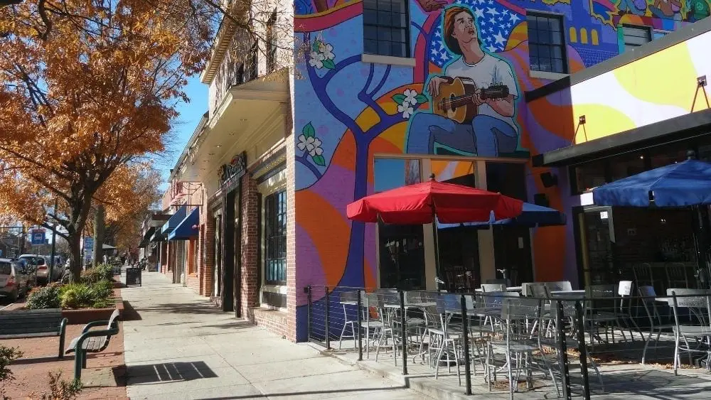 The side of a building painted with a colorful mural of someone playing the guitar; patio chairs are set up in front.