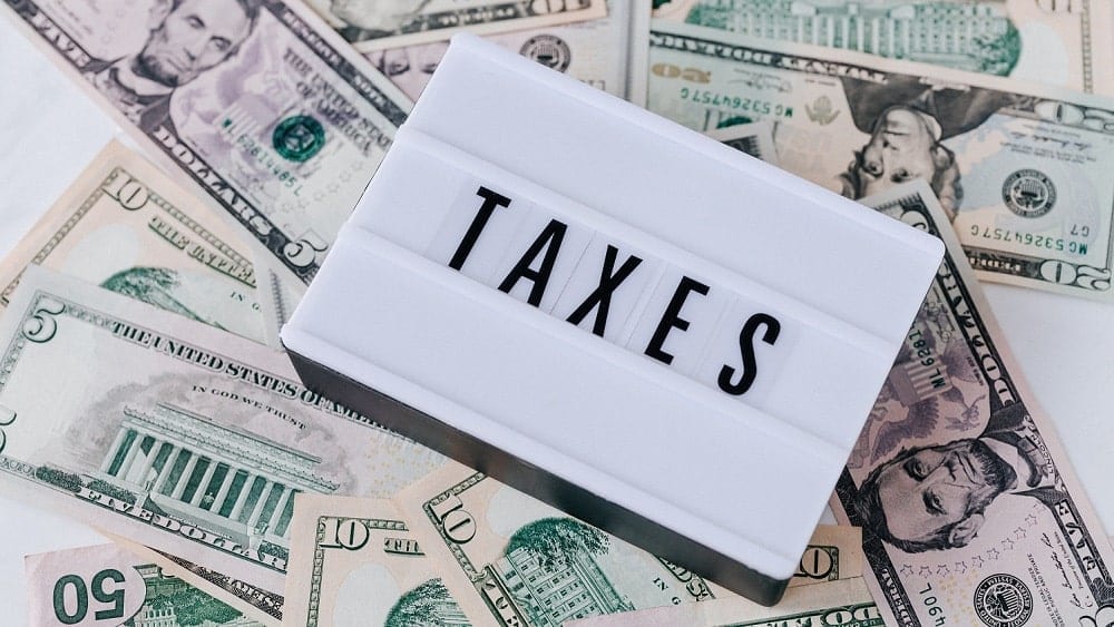 A light box that reads "TAXES" lying on top of a stack of paper money.