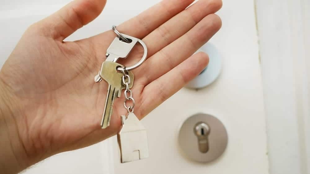 A hand holding a set of keys with a home's front door in the background.