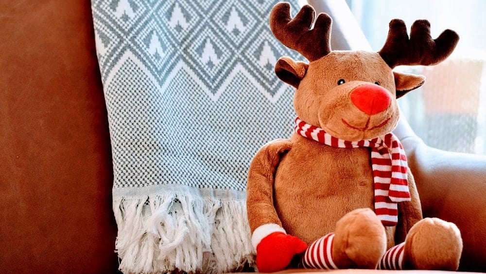 Reindeer stuffed animal sat on chair with a thick throw blanket in the background.