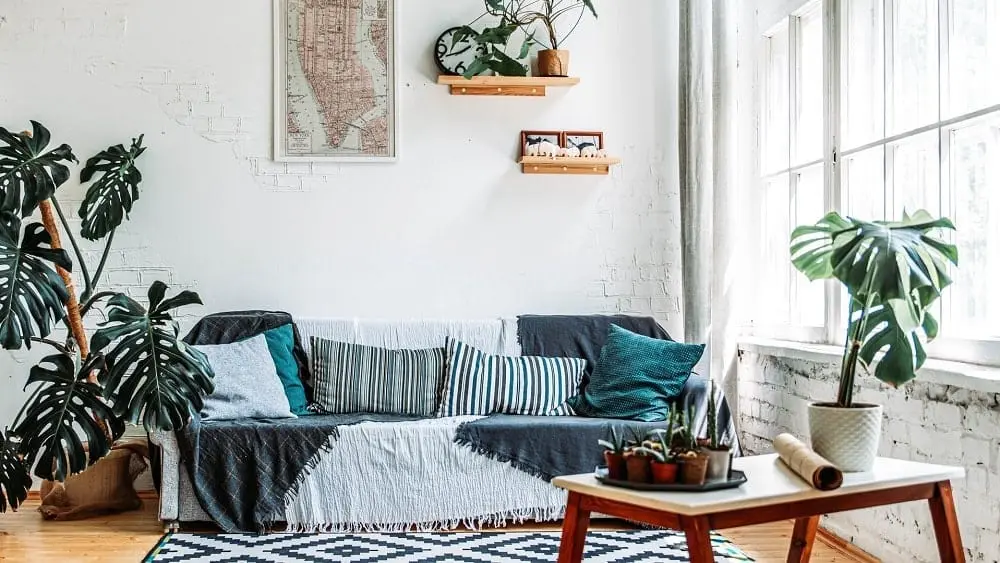 Living room with white brick walls, grey and white rug and sofa, and plants.