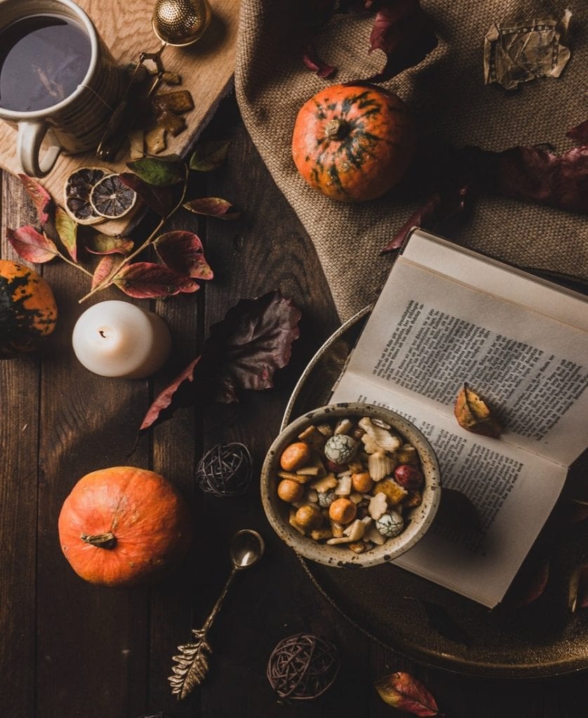 Flatlay of dark wood table decorated with a tea tray, book, candle, fall leaves, and pumpkins.