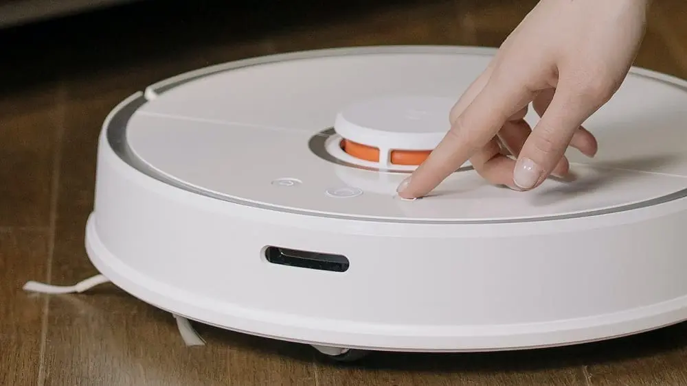 Close shot of person pressing button on a robotic vacuum.