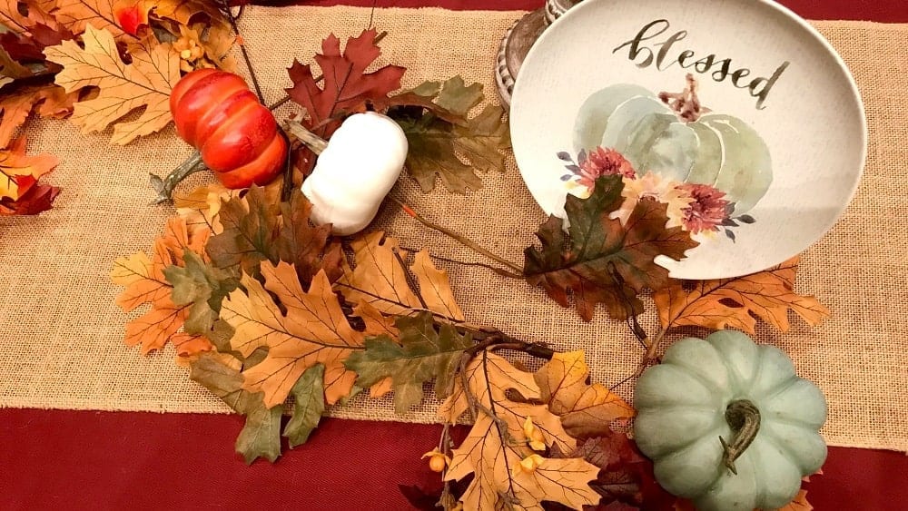 Table decorated with fall foliage, blue, white and orange pumpkins, and a plate painted with the word "blessed" and a blue pumpkin illustration.