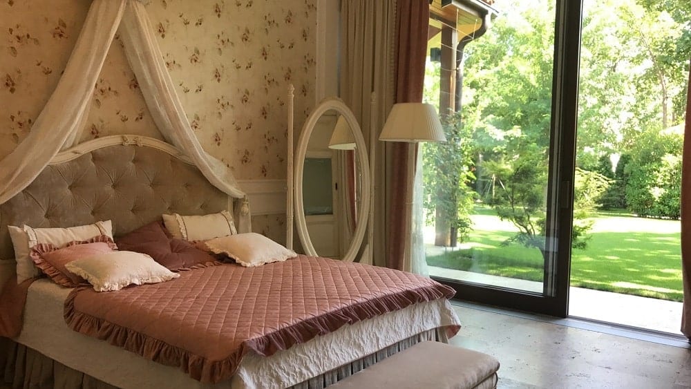 Vintage style bedroom with floral wallpaper, white mirror, and pink and white bed.
