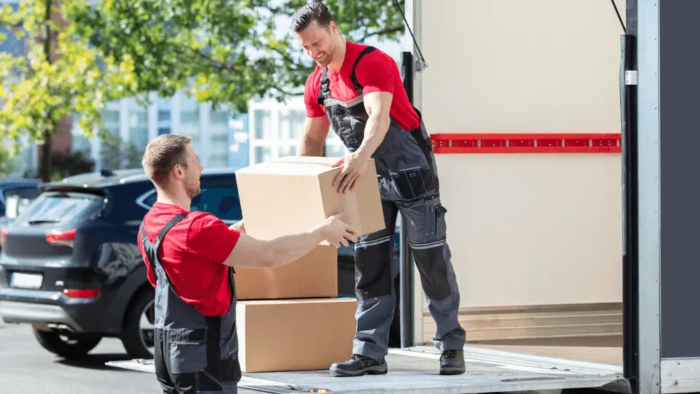 two movers in red and black uniforms move boxes from the back of a moving truck