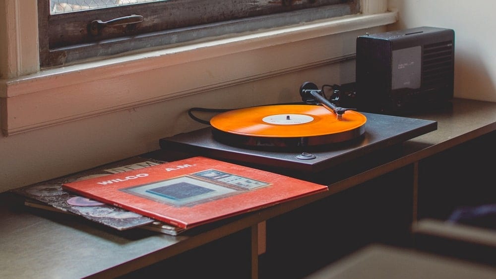 Table with vinyl albums and a record player with an orange vinyl record playing.