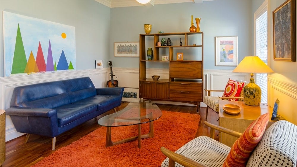 Retro-inspired living room with blue sofa, orange rug, and brown wooden furniture.