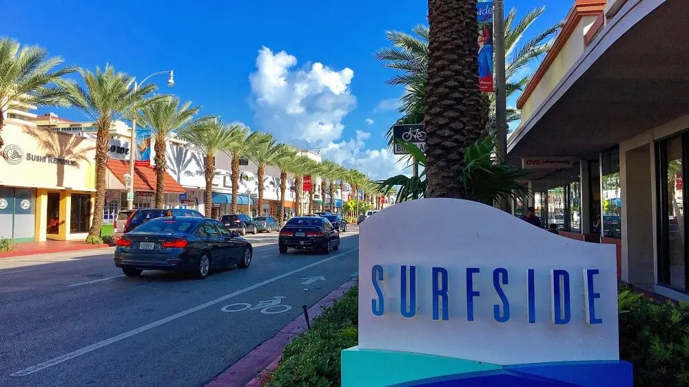 Una calle comercial y un cartel de bienvenida para Surfside, FL.