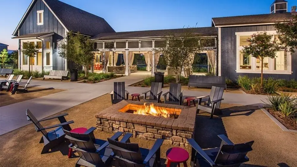 A fire pit with seating surrounding it and a community building in the background.
