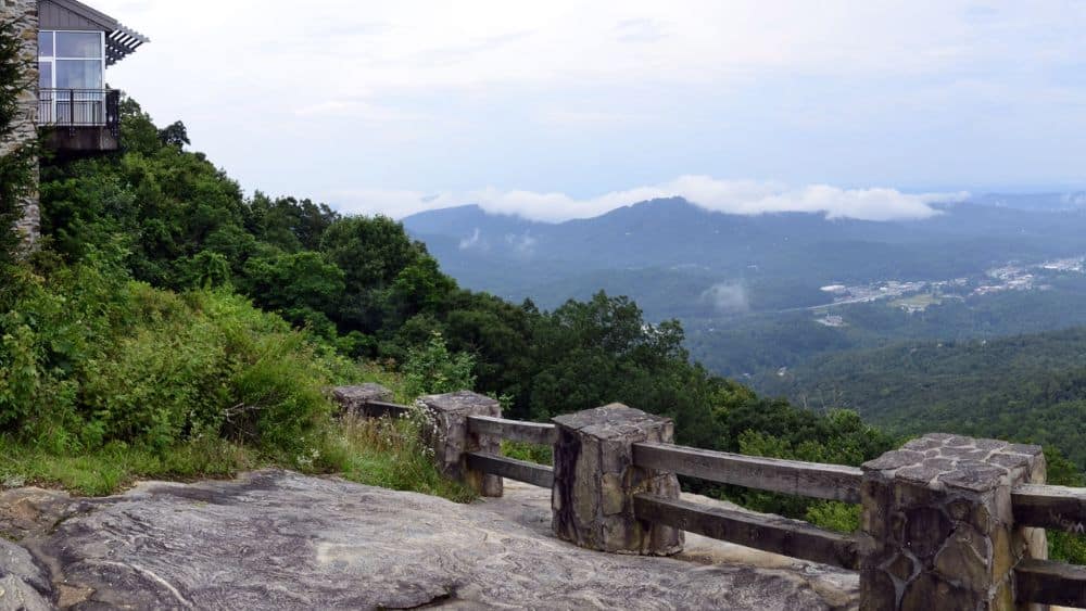 An overlook on a cliff with a stone stone and wood railing. The Blue Ridge Mountains are in the distance.