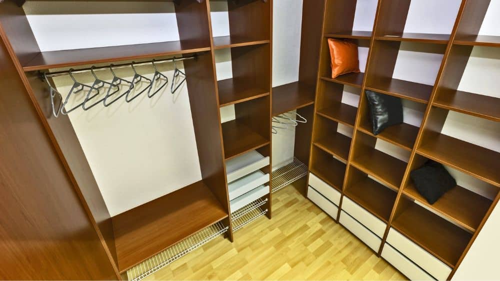 Wooden closet with shelves and hanging rods tucked in a corner.
