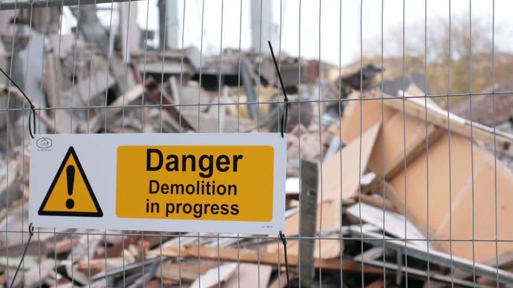 Sign reading "Danger: Demolition in progress" attached to a metal fence.